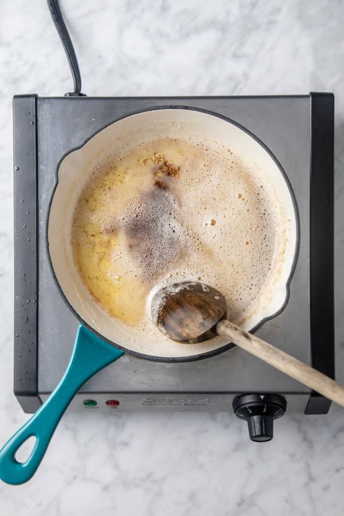 Browned butter being stirred with a wooden spoon in a light colored skillet.