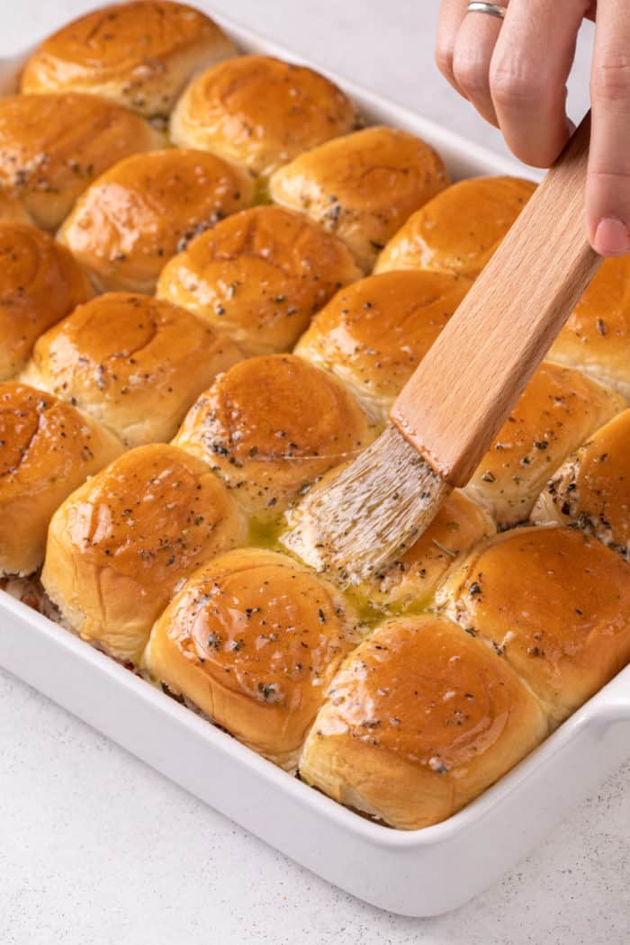 Garlic butter being brushed on top of slider buns for meatball sliders.