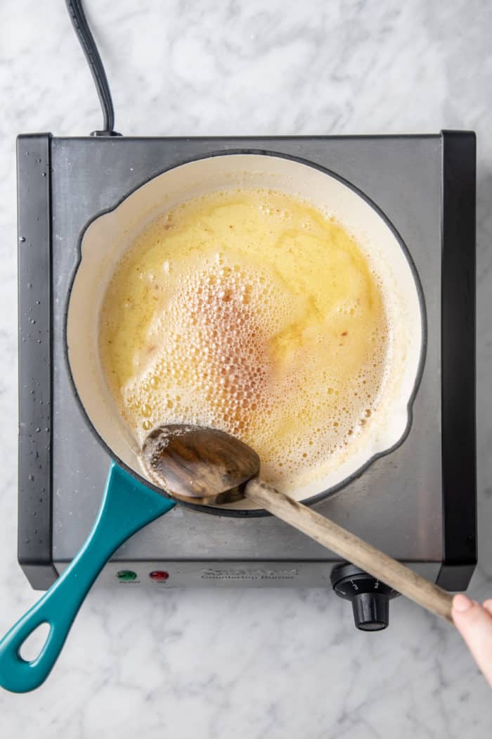 Butter in a light colored skillet that is starting to brown, being stirred with a wooden spoon.