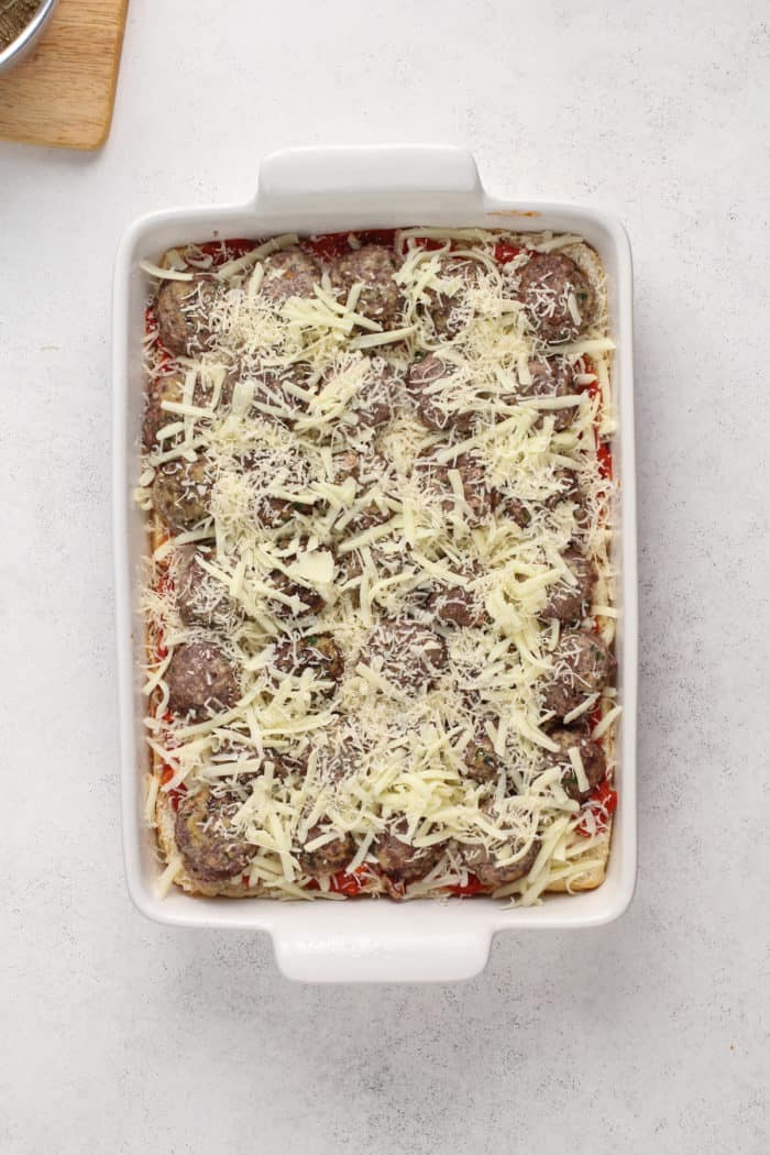 Cheese on top of meatball sliders in a baking pan.