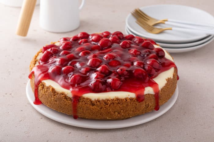 Cheesecake topped with cherry pie filling set on a countertop.