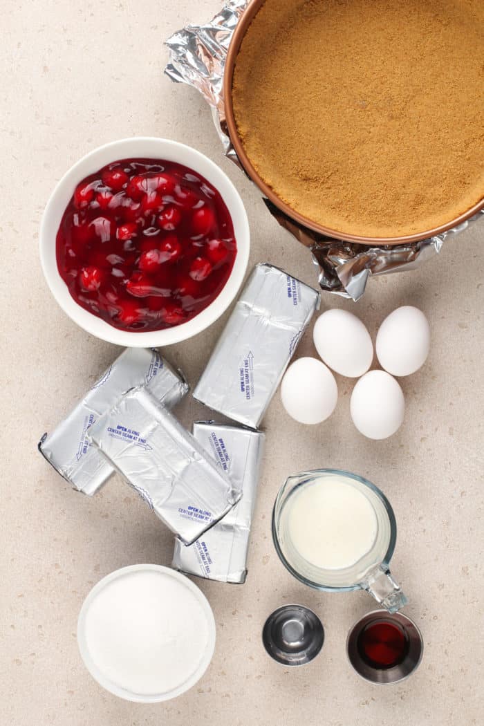Ingredients for cherry cheesecake arranged on a light-colored countertop.