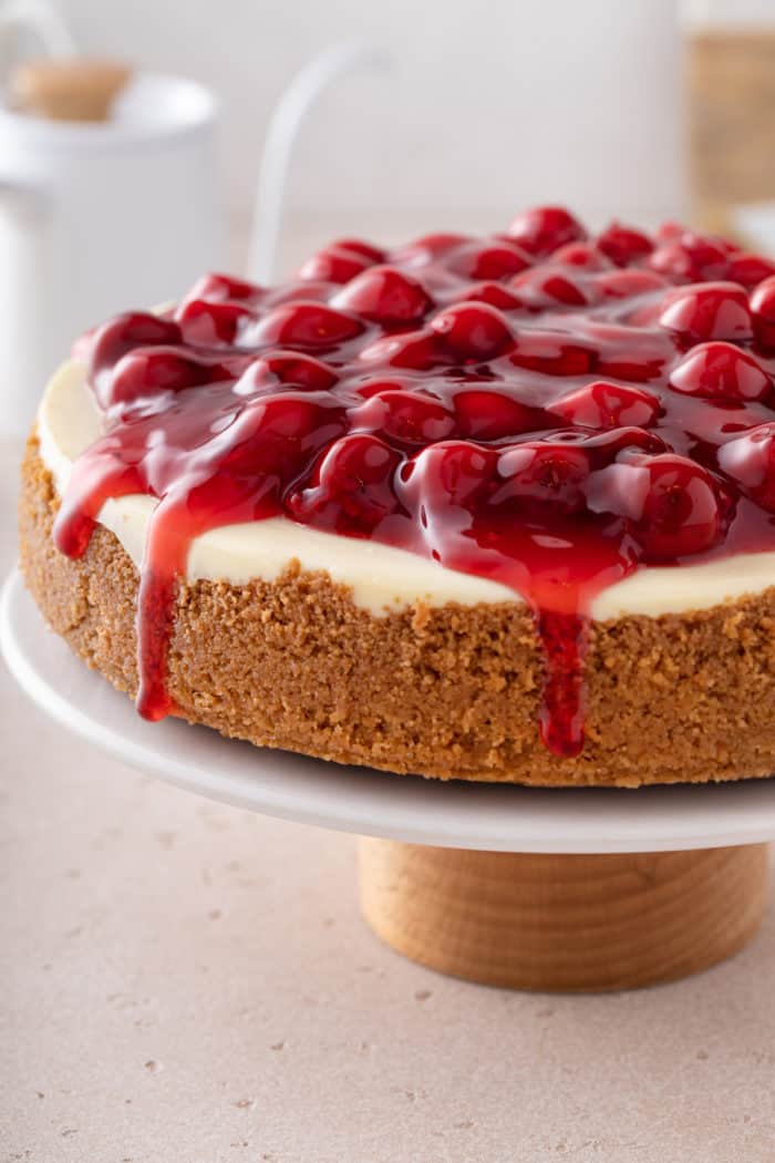 Whole cherry cheesecake set on a cake stand on a countertop.