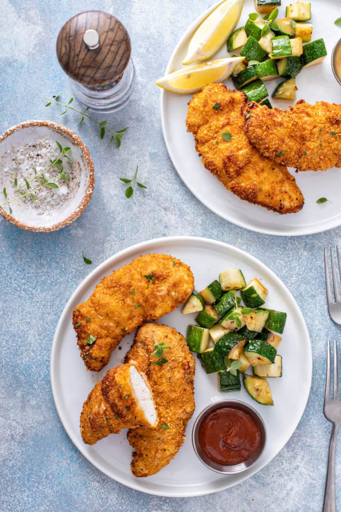 Overhead view of two plates, each with air fryer chicken tenders and sauteed zucchini on the plate.