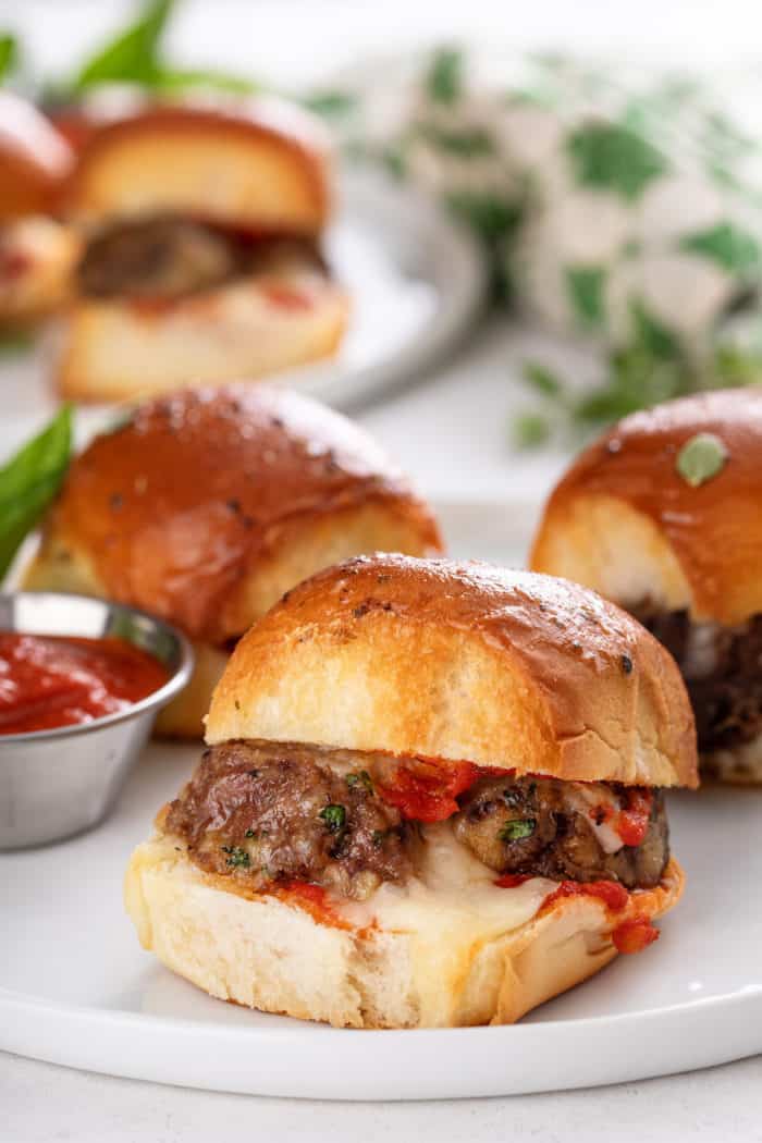 Close up of a meatball slider on a white plate with more sliders in the background.