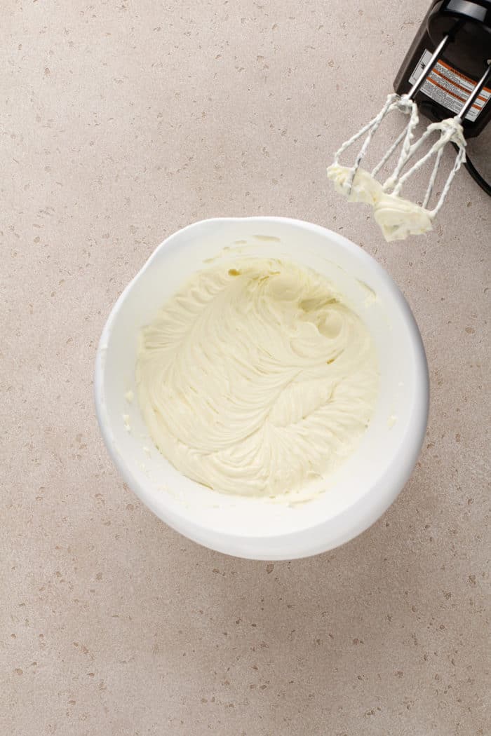 Cream cheese, sugar, and eggs mixed together in a white mixing bowl.