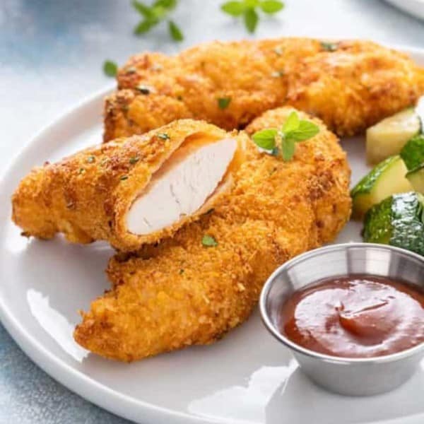 White plate containing air fryer chicken tenders, cooked zucchini, and a ramekin of barbecue sauce.