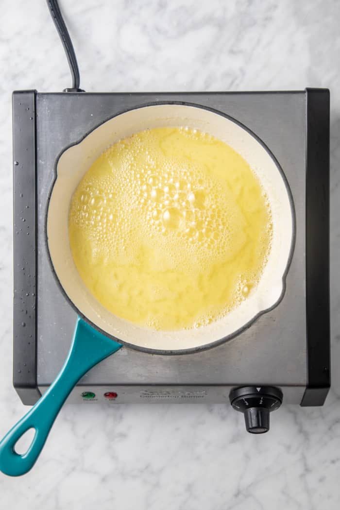 Melted butter that is bubbly and foamy in a light colored skillet over a burner.