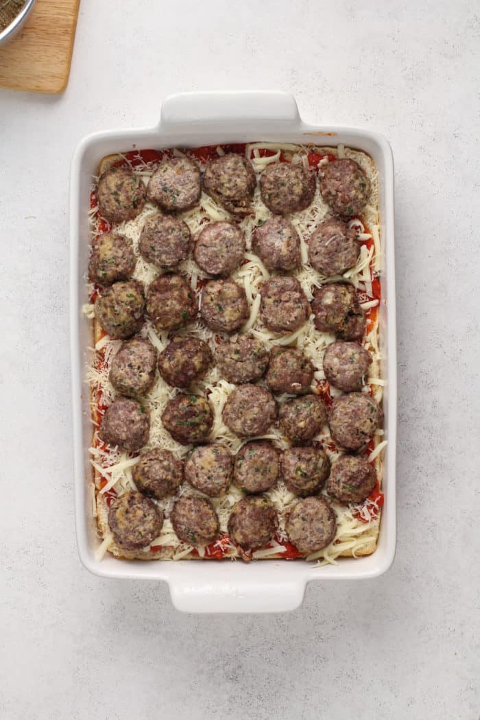 Halved meatballs arranged on cheese-topped slider rolls for meatball sliders.