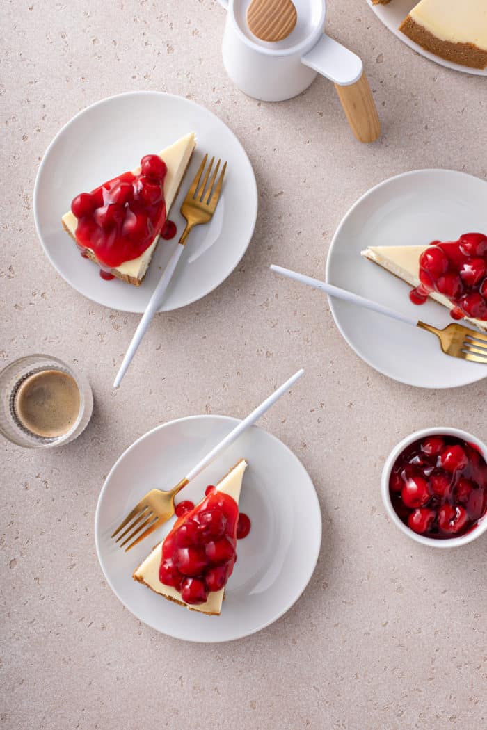 Overhead view of 3 white plates, each with a slice of cherry cheesecake, arranged on a countertop.