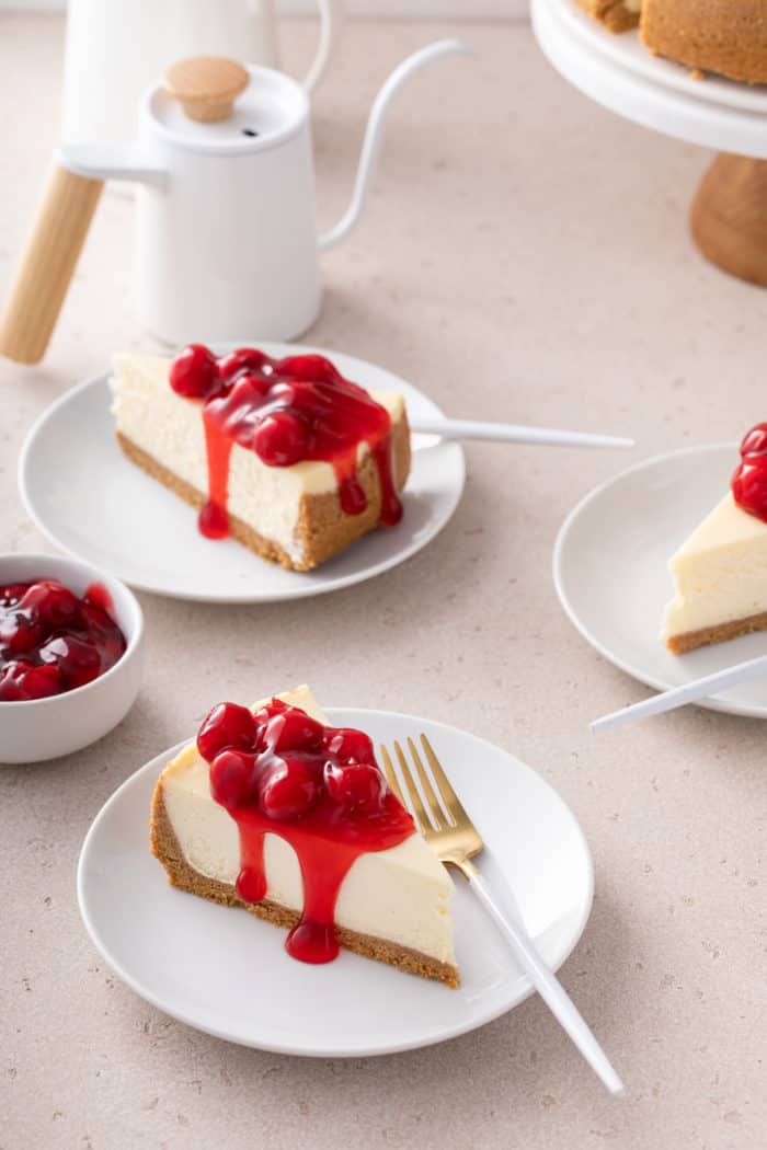 Three slices of cherry cheesecake, each on a white plate, arranged on a countertop.