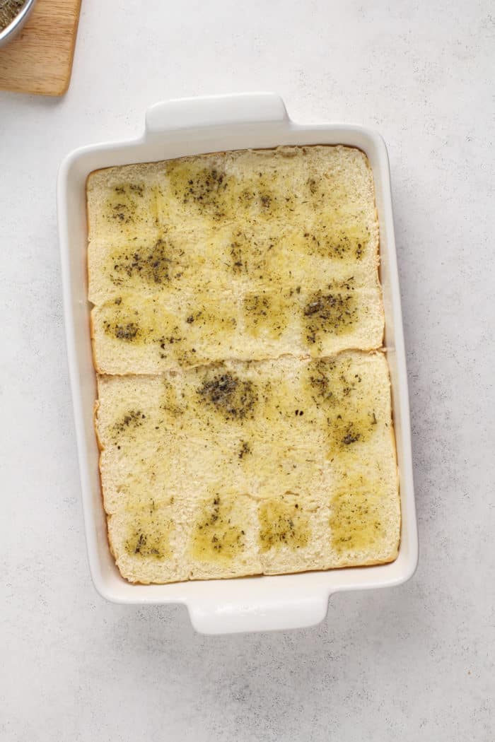 Garlic butter brushed on slider rolls in a baking pan.