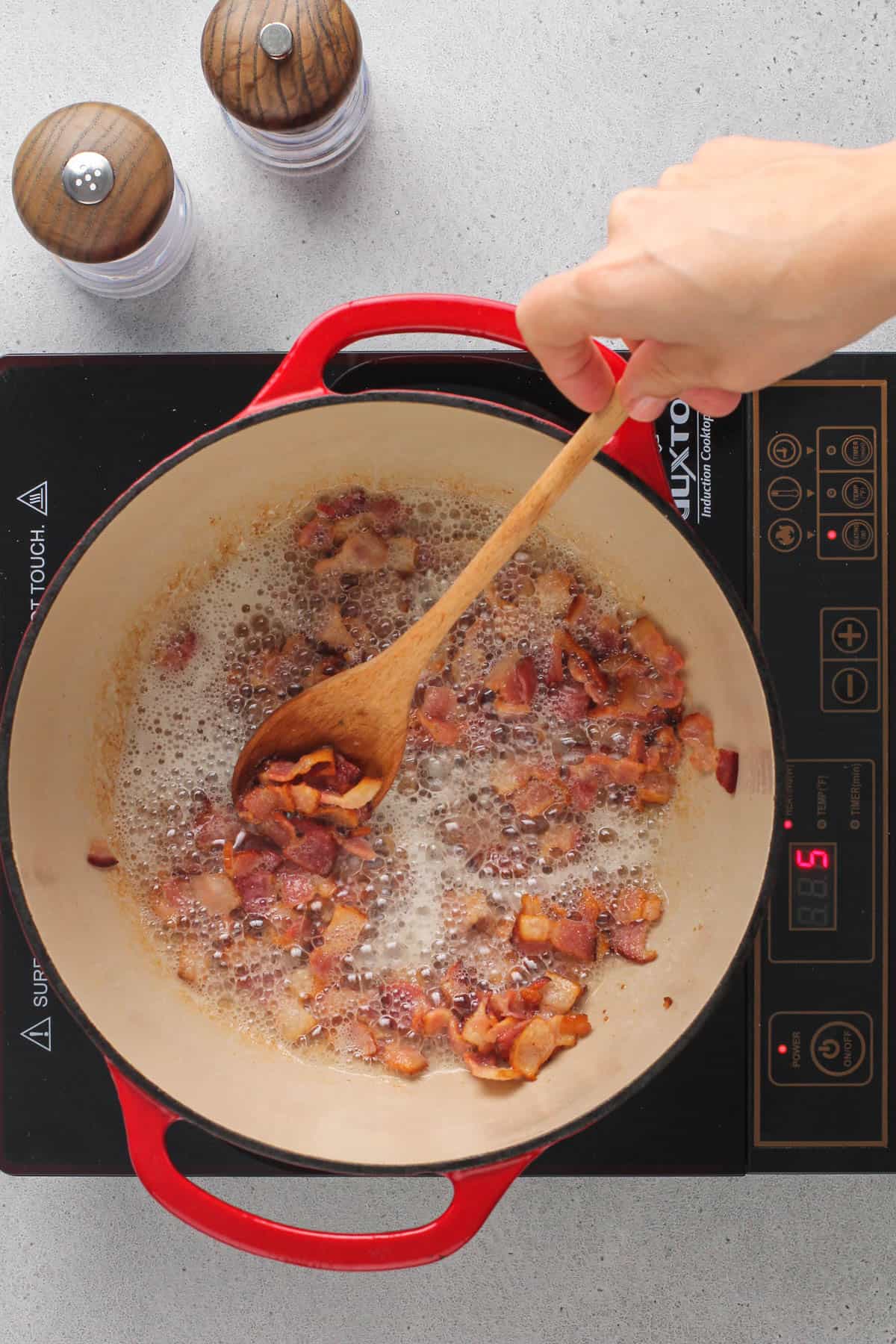 bacon cooking in a red dutch oven