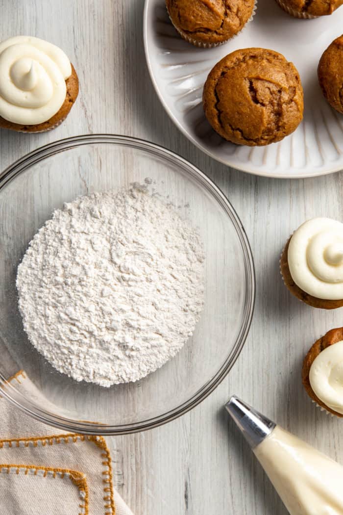 Bowl of cake flour substitute surrounded by cupcakes and frosting.