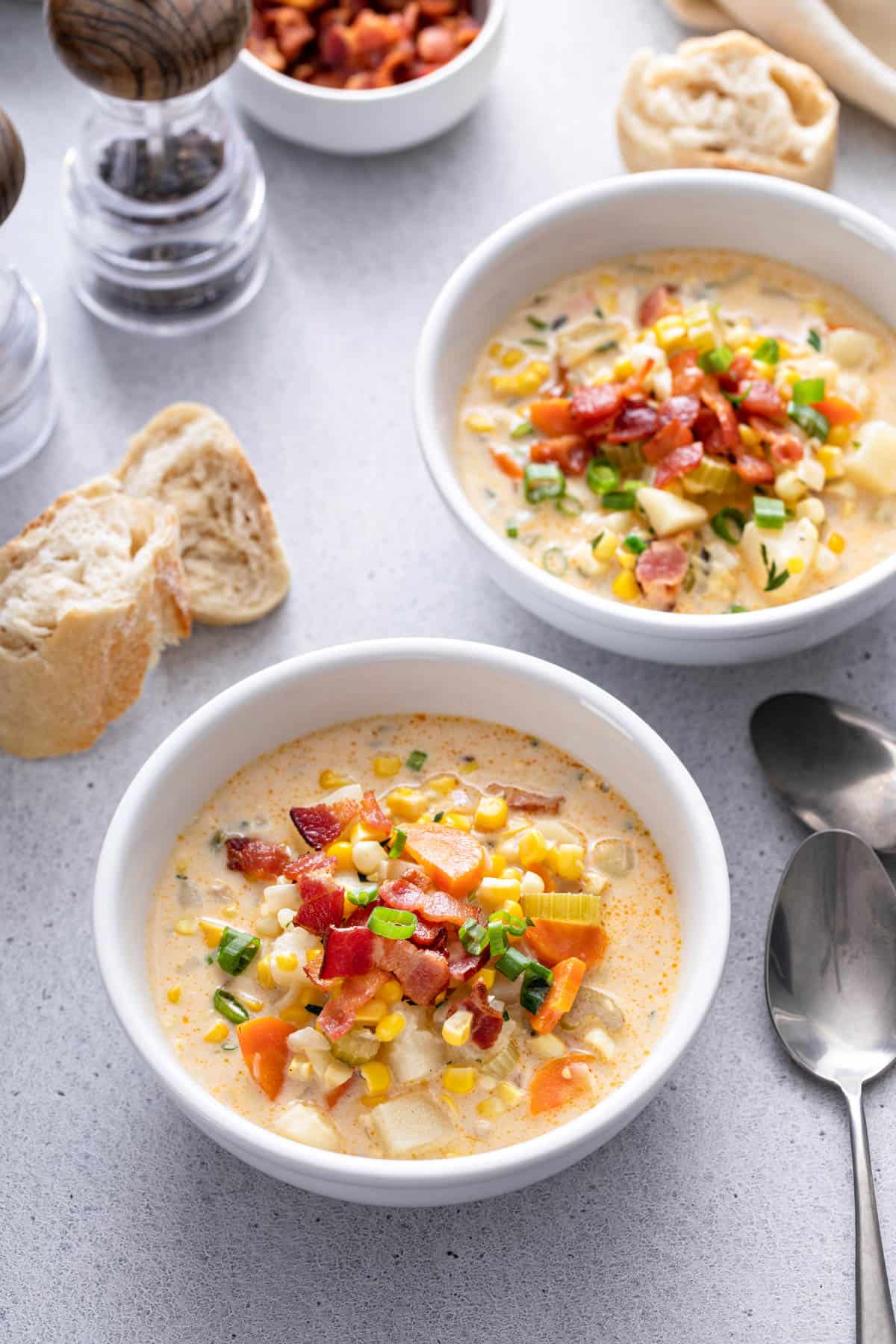 two white bowls of corn chowder on a gray background