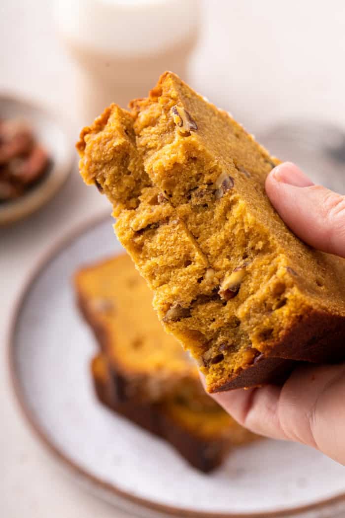Hand holding up two halves of a slice of brown butter pumpkin bread.