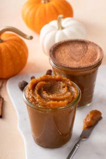 a butter knife or spreader with pumpkin butter on it lies next to a jar