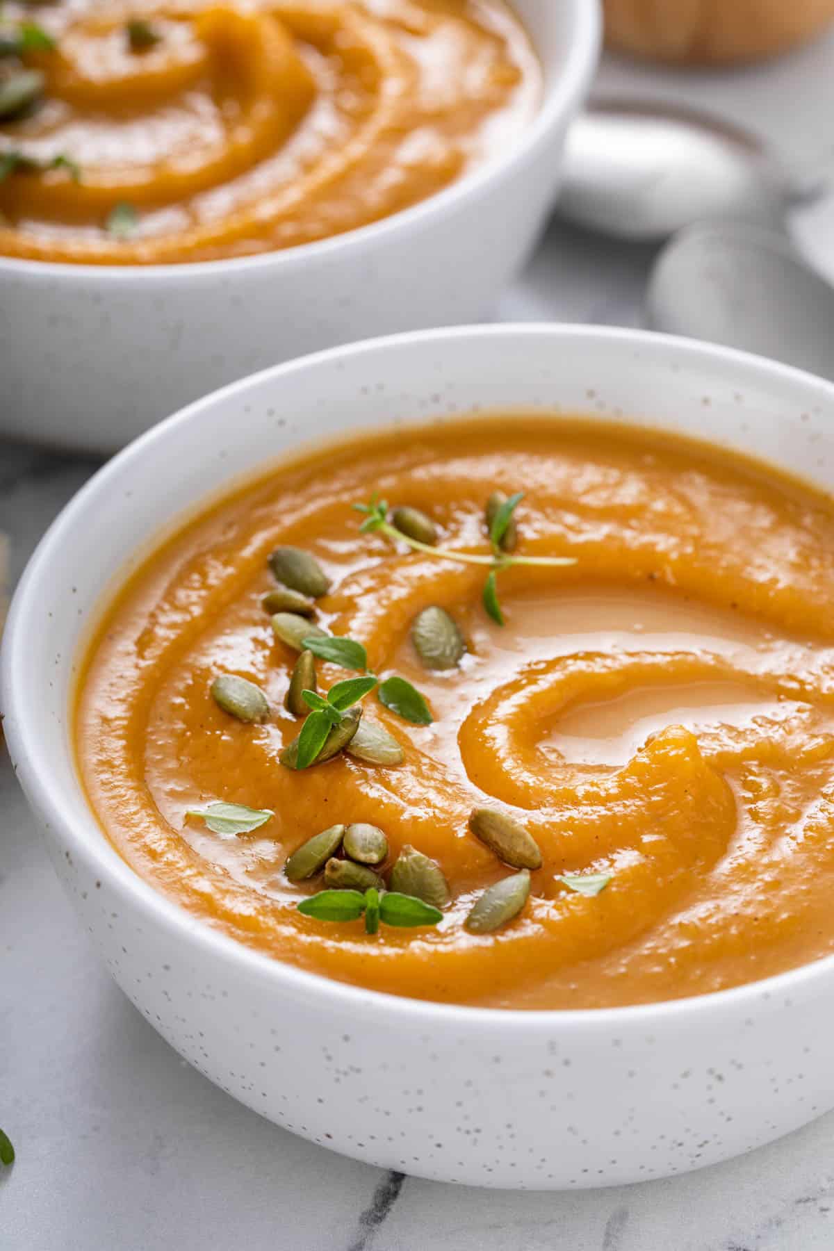 a bowl of butternut squash soup with swirls and toppings