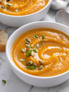 two white bowls of butternut squash soup on a marble background