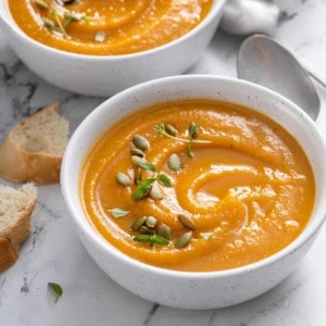 two white bowls of butternut squash soup on a marble background