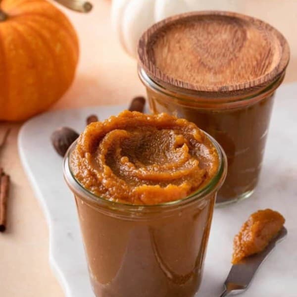 a butter knife or spreader with pumpkin butter on it lies next to a jar