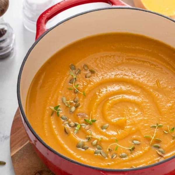 a pot of butternut squash soup resting on a wood trivet