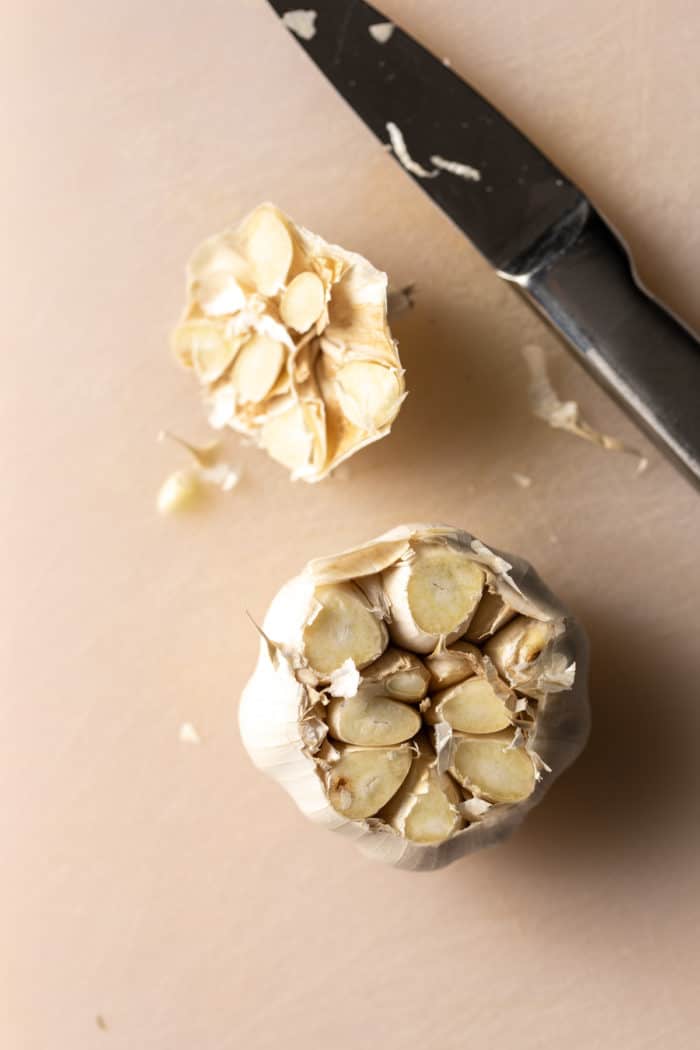 Head of garlic with the top cut off, next to a paring knife.