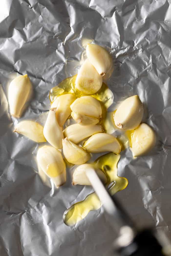 Peeled cloves of garlic on a piece of foil, drizzled in olive oil.