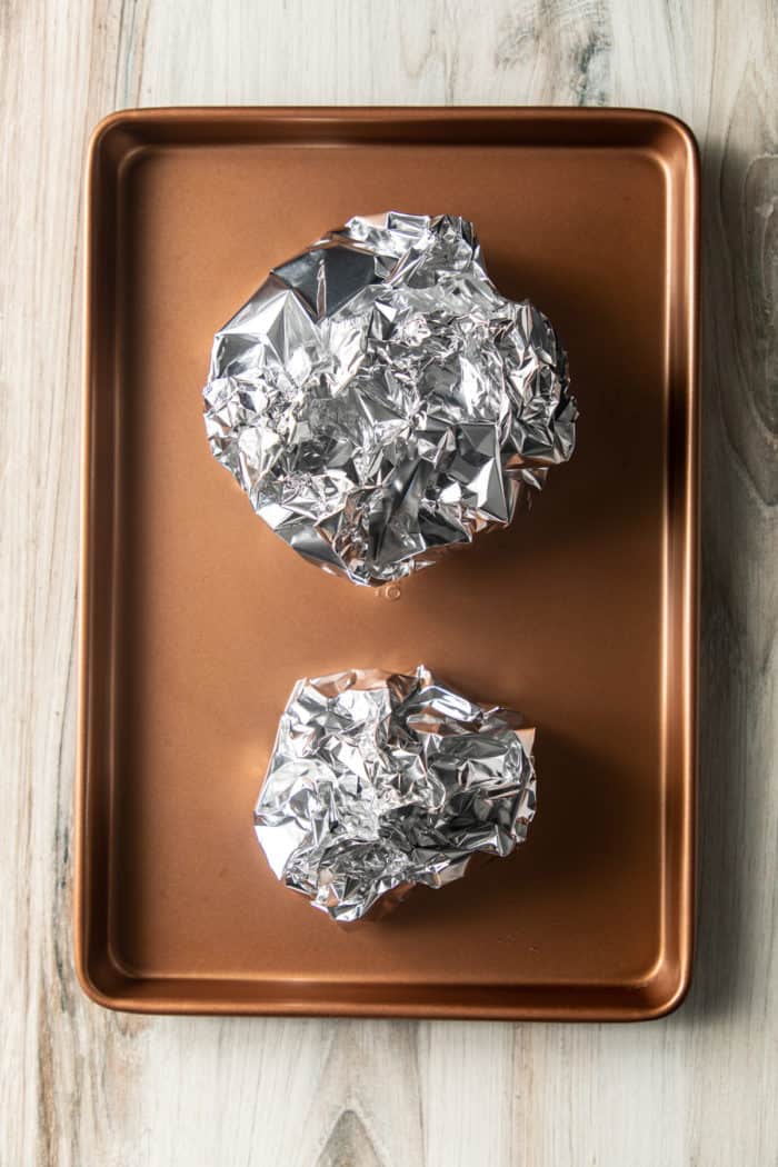 Two wrapped foil packets on a baking sheet.
