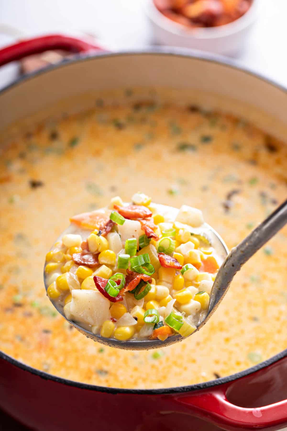 a ladle scooping out corn chowder from a red dutch oven