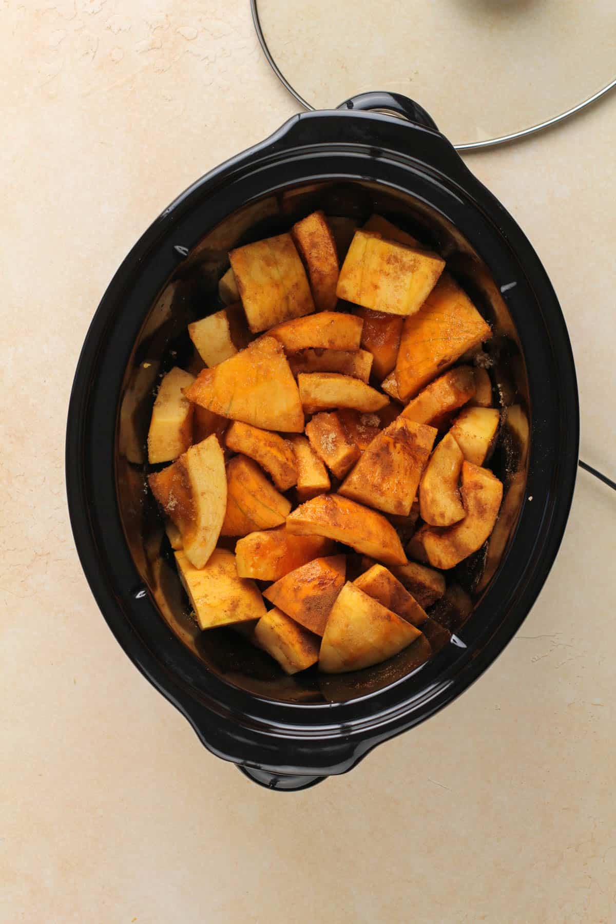 a slow cooker containing pieces of pumpkin, spices, juice and sweeteners for making pumpkin butter