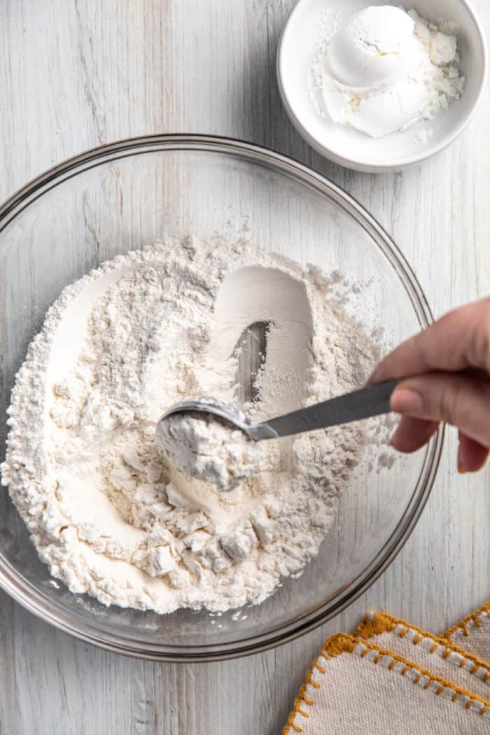 Removing a tablespoon of all-purpose flour from a bowl of all-purpose flour.