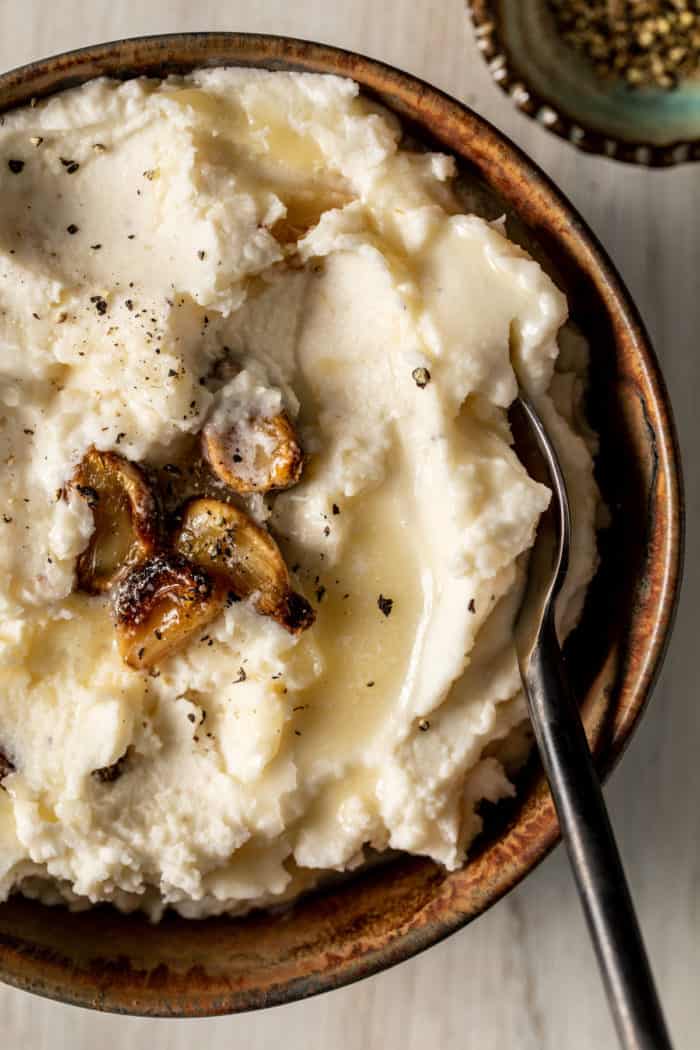 Bowl of garlic mashed potatoes with cloves of roasted garlic on top.