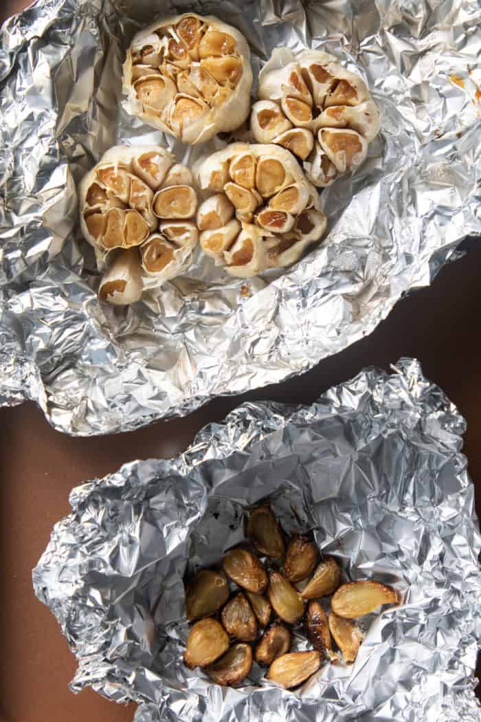 Roasted heads of garlic and roasted cloves of garlic on foil.