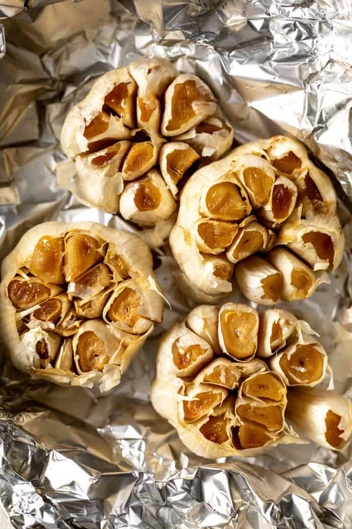 Four heads of roasted garlic on a piece of foil.