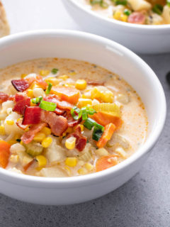 a white bowl with corn chowder and a silver spoon