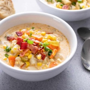 a white bowl with corn chowder and a silver spoon