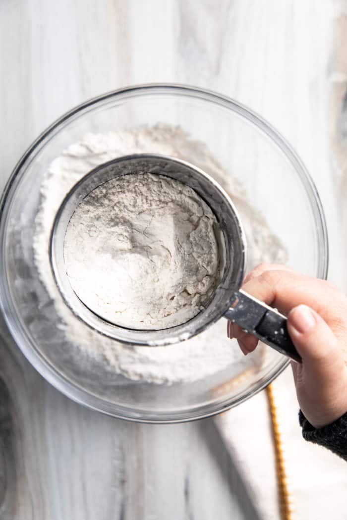 Sifting cake flour substitute using a metal sifter over a glass bowl.