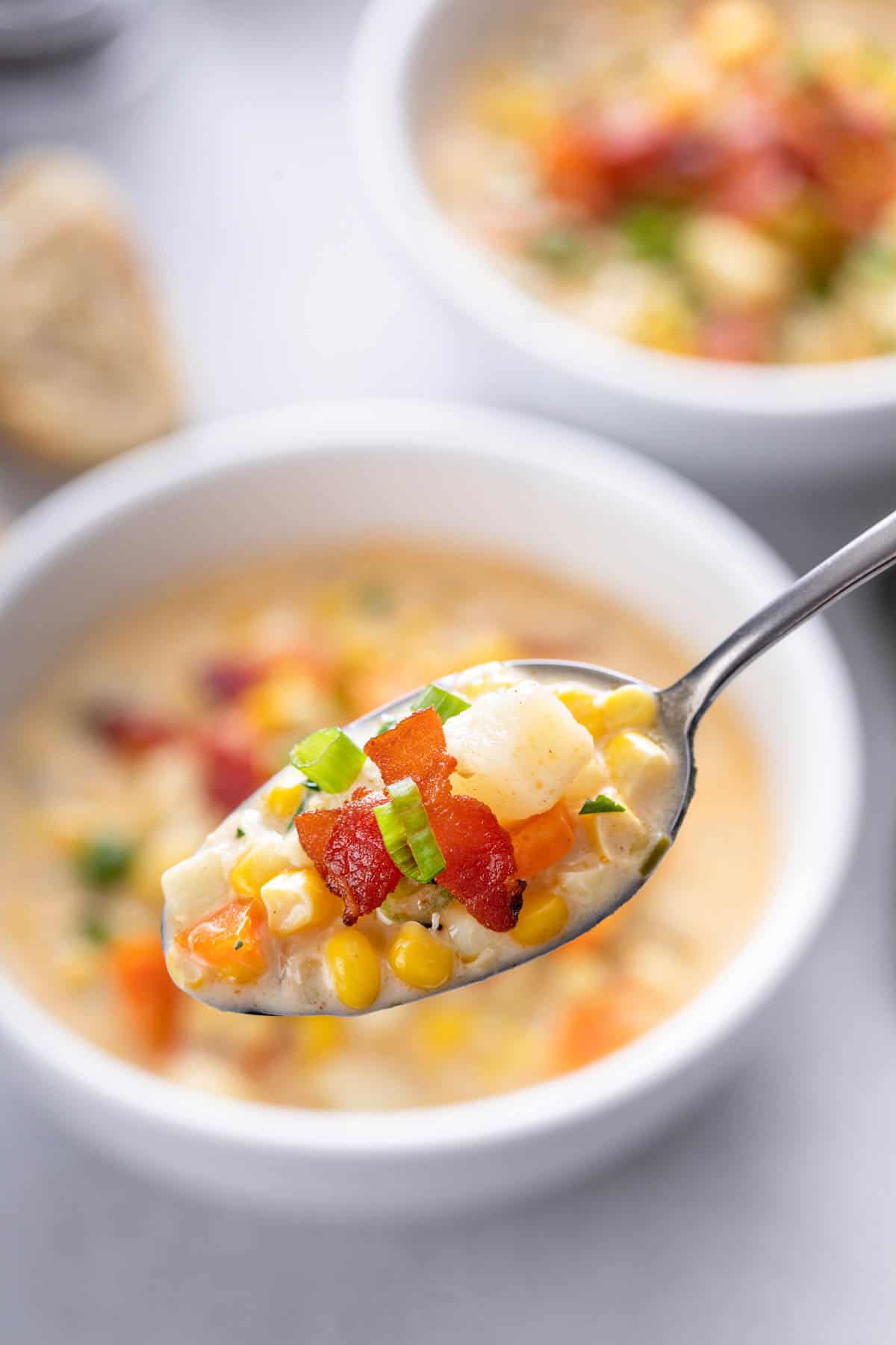 a spoonful of corn chowder in a silver spoon hovering over a white bowl of soup