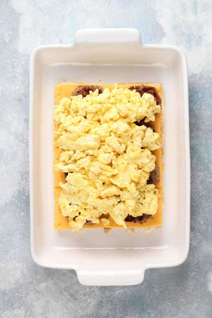 Overhead view of breakfast sliders being assembled in a white baking dish.