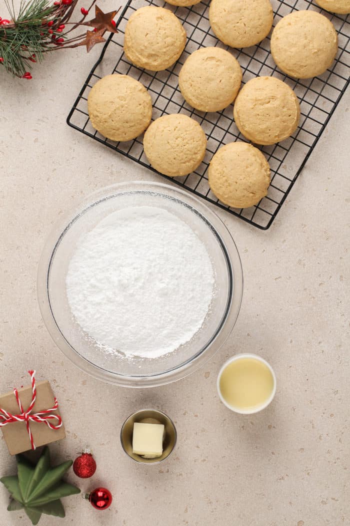 Eggnog icing ingredients next to a wire cooling rack filled with baked eggnog cookies.