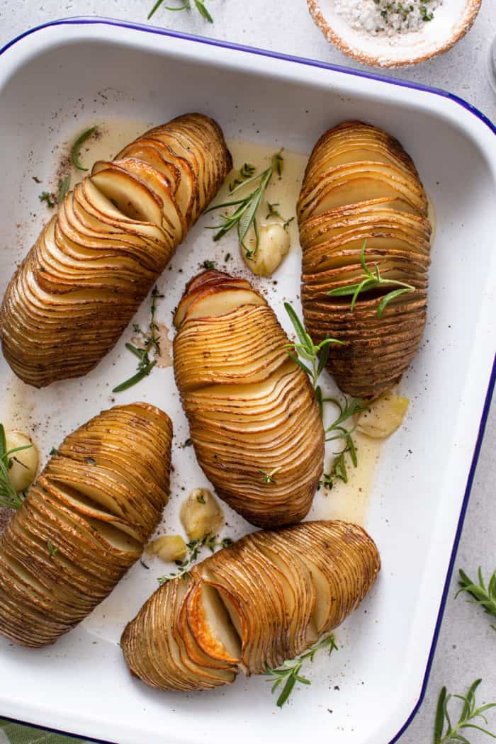 Overhead view of hasselback potatoes garnished with fresh herbs in a white baking dish.