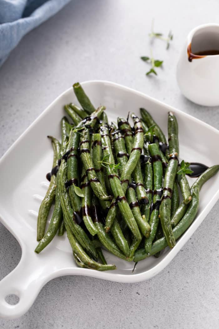 Air fryer green beans drizzled with balsamic glaze on a white dish.