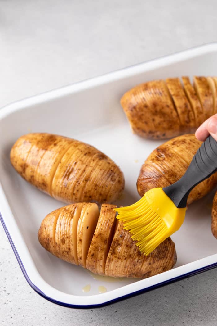 Silicone basting brush basting sliced hasselback potatoes with butter.