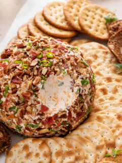 Bacon ranch cheese ball on a platter with a bite taken from it.