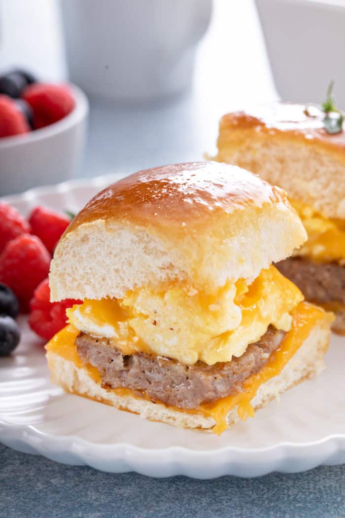 Close up of a breakfast slider on a white plate in front of fresh mixed berries.
