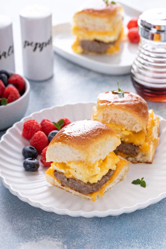 Two breakfast sliders on a white plate next to mixed berries.