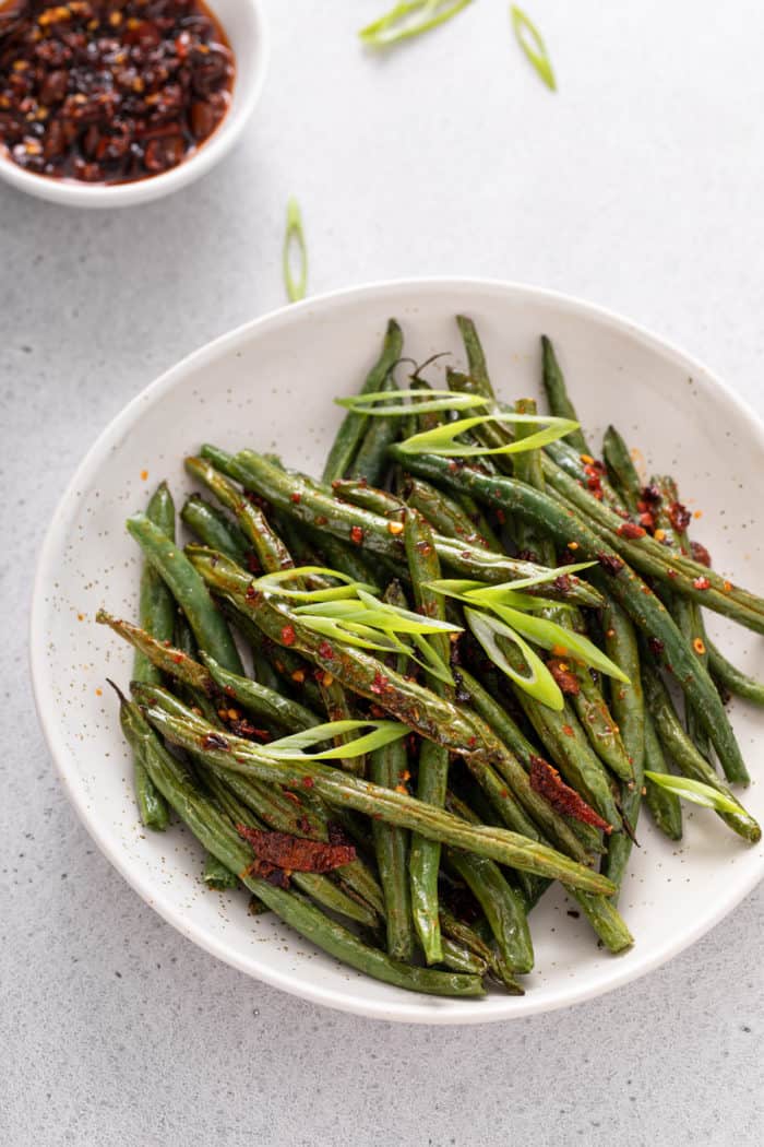 White serving bowl filled with air fryer green beans topped with chili crunch.