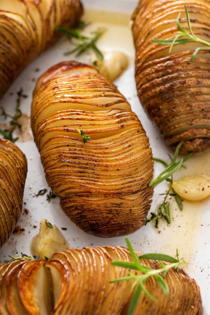 Close up of roasted hasselback potatoes garnished with fresh rosemary sprigs.