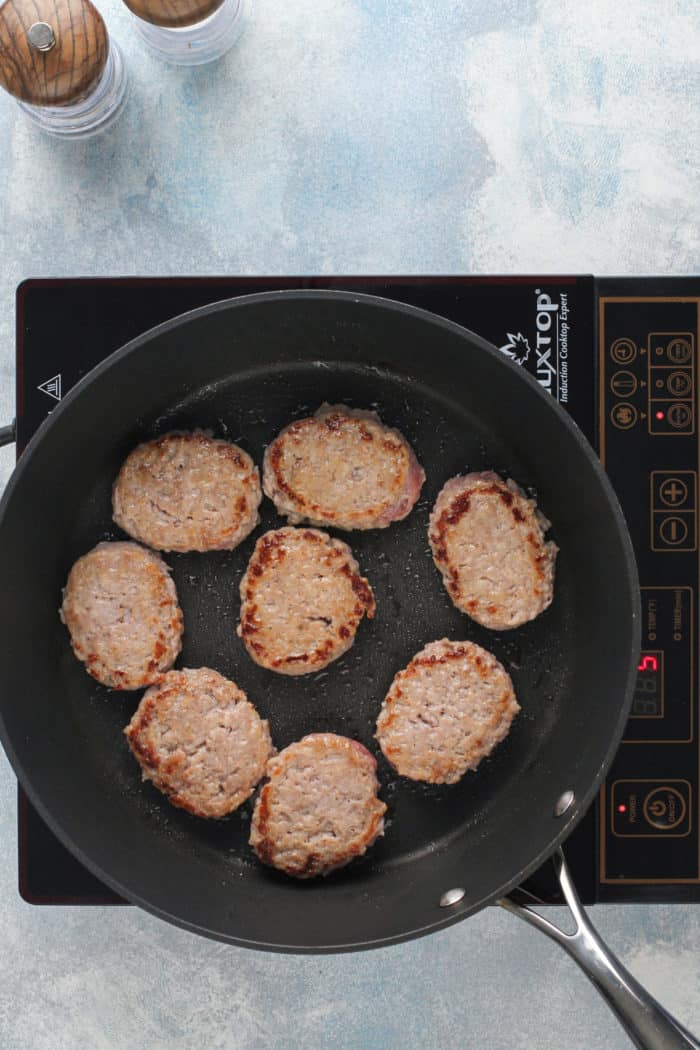 Breakfast sausage patties cooking in a black nonstick skillet.